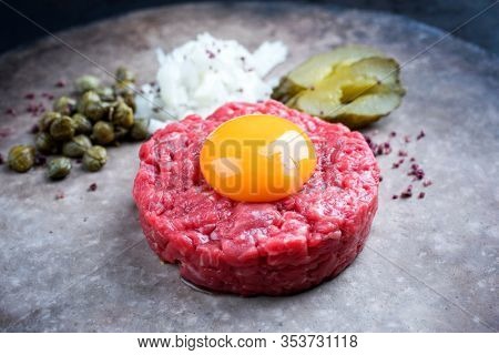 Gourmet tartar raw from beef fillet with yellow of the egg and gherkin with capers and onion as closeup on a modern design plate 