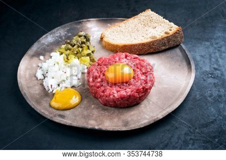 Gourmet tartar raw from beef fillet with yellow of the egg, gherkin and farmhouse bread as closeup on a modern design rustic plate 