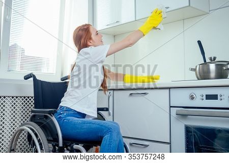 Young Redhaired Ginger Disabled Woman In Wheelchair Wearing Yellow Ribon Gloves And Cleaning Apartme