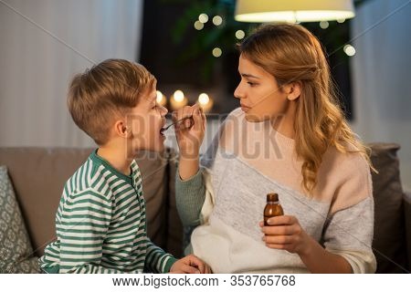 family, health and people concept - sad mother giving antipyretic medication or cough syrup to ill little son at home
