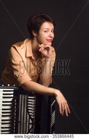 A Brunette In A Gold Shirt, With Short Haircut, On A Dark Kground Of The Studio. With Accordion Musi