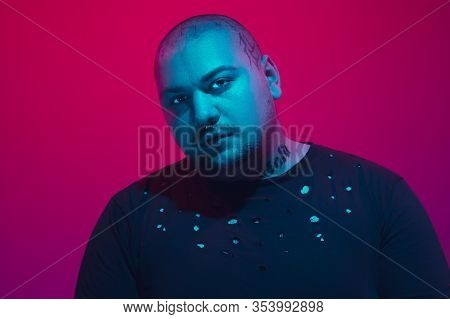 Portrait Of A Guy With Colorful Neon Light On Red Studio Background. Male Model With Calm And Seriou