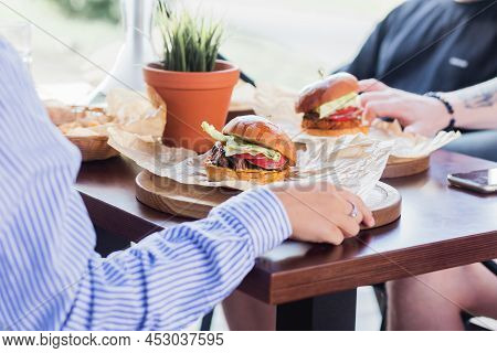 A Company Of Friends Met For Lunch In A Summer Cafe, Chatting And Eating Burgers. Fast Food In Resta