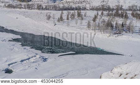 A River In A Snowy Valley. The Shores Are Icy. Steam Is Visible Above The Ice-free Turquoise Water. 