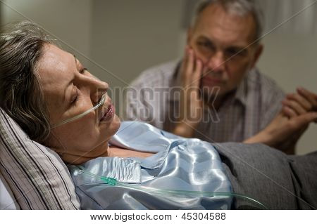 Nemocný zralá žena ležela v posteli starosti manžel drží za ruce