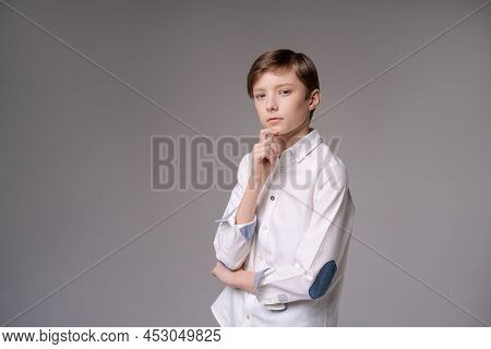 Thoughtful Young Teen Man Holding Hand On Chin Indecision Pose In White Shirtisolated On Gray Studio