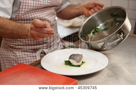 Chef sert bouillis bar (branzino) avec des herbes, léger mouvement flou sur cuillère