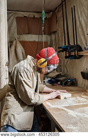 Vertical Shot Of Young Man Wearing Safety Glasses And Earmuffs Shaping Wooden Detail Using Benchtop 