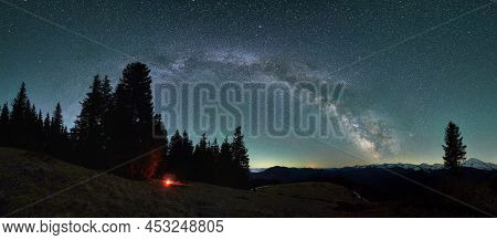 Panoramic View Of Evening Mountain Hills Under Beautiful Starry Sky. Small Flame, Silhouette Of Tent