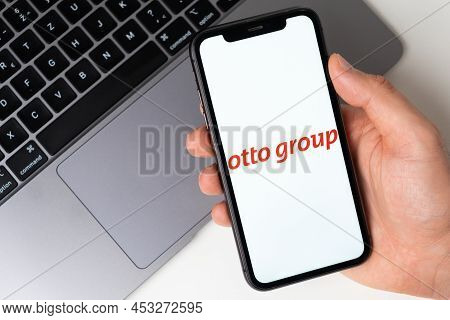 Otto Group App On The Screen Of Smartphone In Mans Hand With A Laptop On The Background. Online Shop