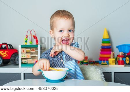 Toddler Boy Eats With Spoon And Is Covered In Food. Baby Food, Food Allergies, Self-feeding.