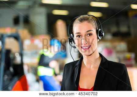 Amichevole donna, dispatcher o supervisore tramite auricolare nel magazzino dell'azienda, sorridente di inoltro