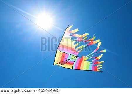 Big Colorful Kite Flying In The Blue Backlit Sky And The Glow Of The Sun At Noon