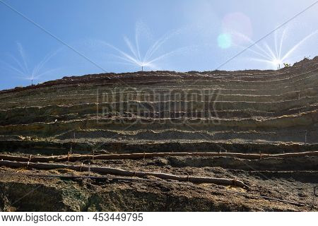 Irrigation System Sprinklig Water On Newly Developed Leveled Slope. Sprays Of Water Across Blue Sky 