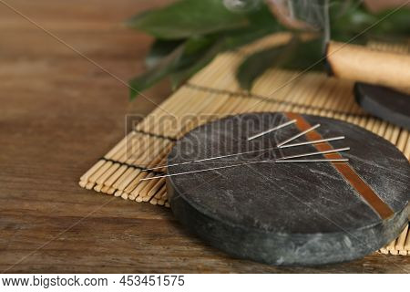 Grey Stone Coaster With Acupuncture Needles On Wooden Table. Space For Text