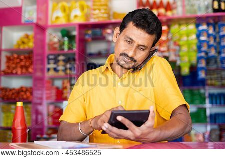 Kirana Or Grocery Marchant Calculating Order Price While Taking On Mobile Phone From Customer - Conc