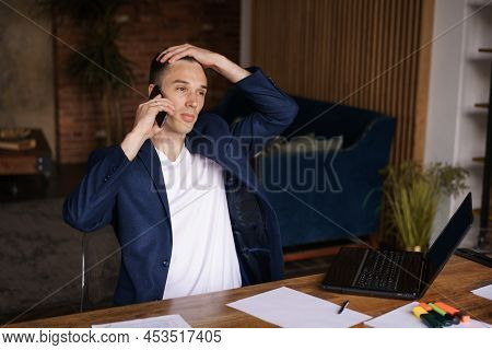 Very Busy. Confident Successful Man In Jacket Working On Laptop And Talking On Phone While Sitting A