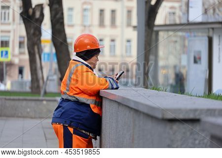 Moscow, Russia - April 2022: Woman Worker Standing With Smartphone In A City. Rest During Street Cle