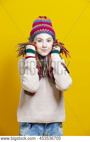 Winsome Caucasian Blond Girl In Warm Knitted Hat And Scarf Posing With Lifted Hands While Touching C