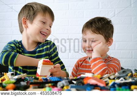 Two Boys Sit Down At The Table And Assemble The Designer. Children Laugh, Are Joyful, They Have Fun 