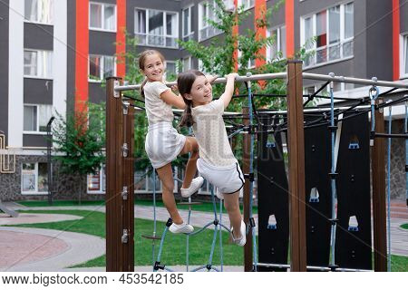 Two Pretty Teen Girls Playing On A Modern Playground In Identical Clothes. Sister, Bffs. Sisterhood,