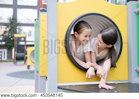 Kids Outdoors Having Fun On Modern Playground With New Colorful Equipment. Sisterhood, Friendship. T