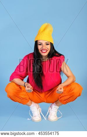 Widely Smiling Young Woman In A Bright Multicolored Casual Style Clothed Sitting On Hunkers Over Blu
