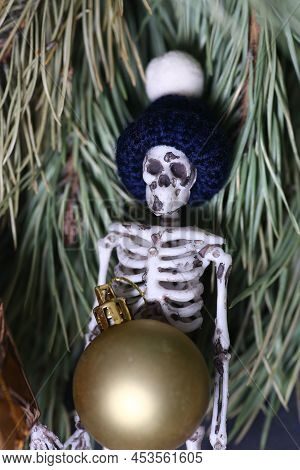 Christmas Concept - Funny Skeleton In Skully Hat With Christmas Ball Against Fir Tree Background