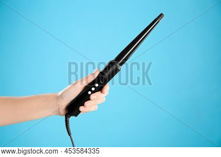 Woman Holding Clipless Curling Hair Iron On Light Blue Background, Closeup