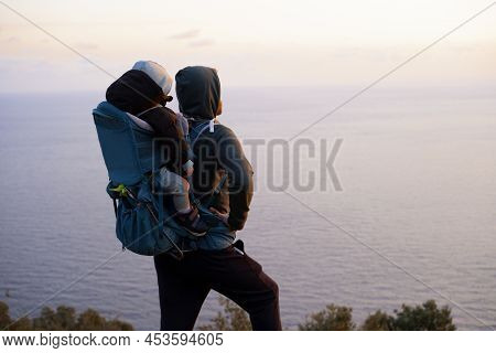 Young Caucasian Man Hiking Near Beautiful Blue Sea Carrying Baby In Bacpack, Sling, Carrier.family T