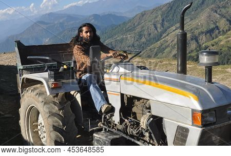 A South Asian Bearded And Long Haired Man Looking At Camera While Driving An Old Tractor In Hilly Ar