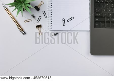 Working Place With Grey Laptop With Black Buttons, White Notebook And Paper Clips On It, Gold Colore