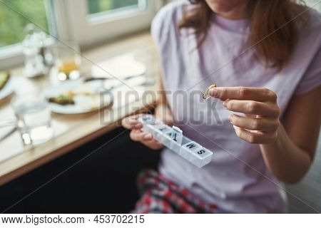 Focus On Foreground Of Pill In Hand Of Partial Girl With Blurred Background Of Food On Table Of Wind
