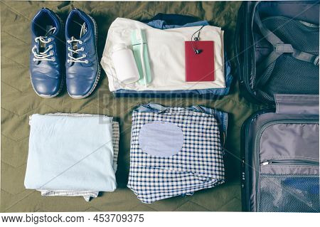 Stacked Clothes, A Passport, A Pair Of Shoes, And A Toothbrush Next To An Open Suitcase