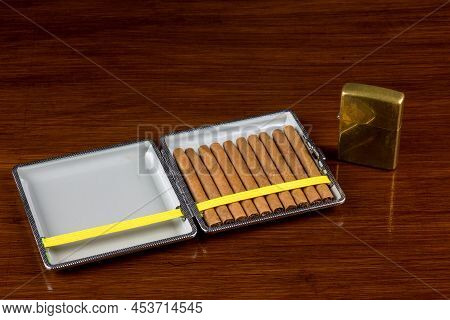 Small Cigars In Cigar Case On Old Varnished Wooden Surface With Old Brass Lighter