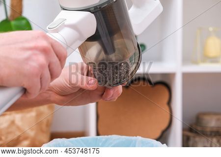 A Man Shakes Out A Trash Container Of A Wireless Vertical Vacuum Cleaner Into A Trash Can. The Conta