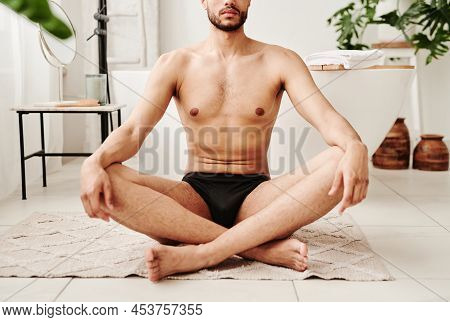 Close-up Of Young Shirtless Man Sitting On Carpet In Lotus Position And Doing Yoga In Bathroom