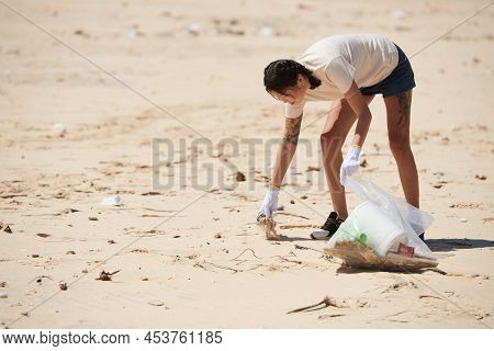Young Woman Wearing Textile Gloves When Picking Up Trash On Sandy Beach On Earth Day