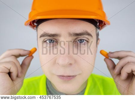 A Worker In A Hard Hat And Green Vest Puts On Ear Plugs. Industrial Safety. Industrial Noise Protect