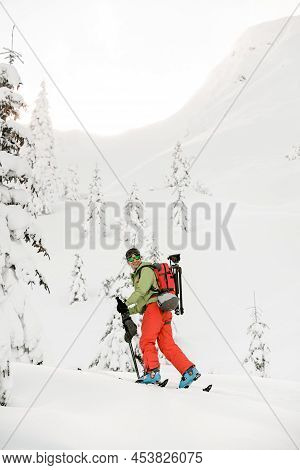 Happy Skier In Bright Jacket Is Climbing The Hill Using Skitour Equipment.
