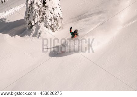 Active Snowboarder In Bright Multicolored Overall Riding Down On Splitboard Splashing Snow
