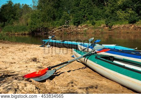 Tourist Canoes With Paddles Stand On The River Coast In Summer On A Water Hike. Rafting On Inflatabl