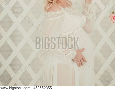 Pregnant Woman Inwhite Dress Caressing Her Belly In Studio