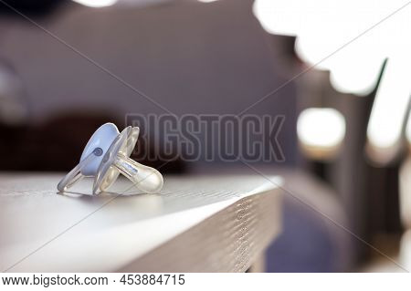 A Portrait Of A Soother Lying On A Wooden Table Indoor In A Living Room. The Pacifier Is White And S