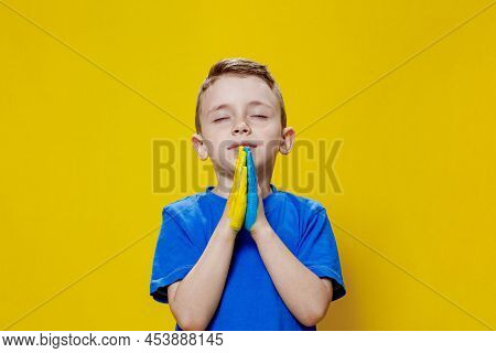 Ukrainian Boy Prays For Ukraine. Children Against War. A Boy In A Blue T-shirt On A Yellow Backgroun