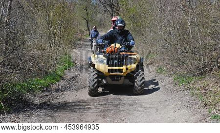 A Couple On A Yellow Quad Bike Riding On A Dirt Road In The Spring Forest. Front View. Extreme Type 