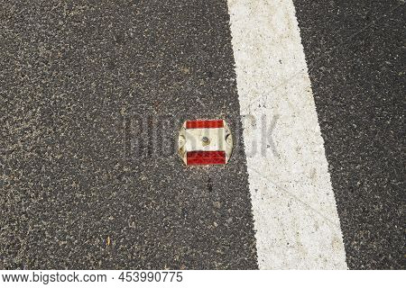 Metal Road Stud With Red Reflector On Asphalt Road With White Painted Lane Marking Line As Divider O