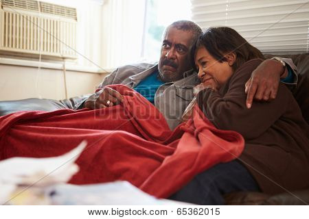 Senior Couple Trying To Keep Warm Under Blanket At Home