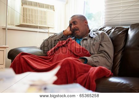 Senior Man Trying To Keep Warm Under Blanket At Home