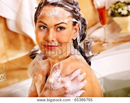 Happy woman washing hair in bubble bath.